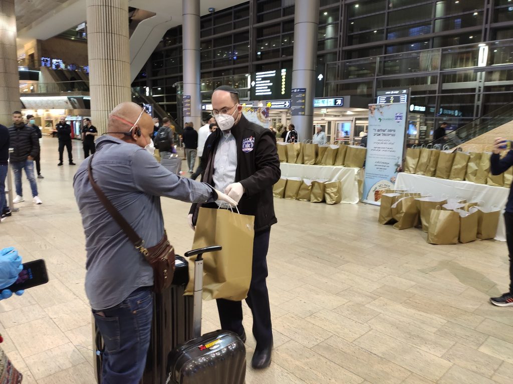 מתי גולדשטיין מתנדב זקא מחלק ערכת ליל הסדר לנוסע שחולץ מניגריה